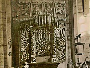 Fragment of aron-kodesh. In the center 2 lions hold Menora, against the background of a double-headed eagle. At the edges you can see the heads of this eagle, crowned with crowns.
At the top are animals with 4 species of plants, symbols of the festival of Sukkot: the bear with etrog, the eagle with lulav (palm leaves), the deer with adas (myrtle) and the lion with arava (willow)